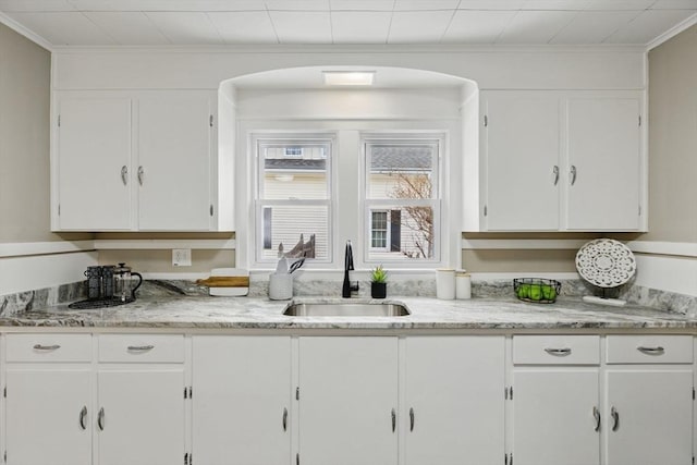 kitchen with light stone counters, arched walkways, ornamental molding, white cabinets, and a sink