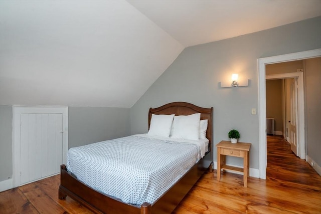 bedroom with radiator heating unit, wood finished floors, and lofted ceiling
