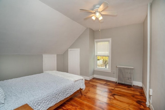 bedroom featuring hardwood / wood-style floors, baseboards, vaulted ceiling, radiator heating unit, and a ceiling fan