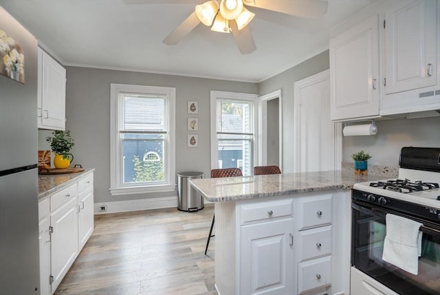 kitchen featuring freestanding refrigerator, under cabinet range hood, range with gas cooktop, light wood finished floors, and a peninsula