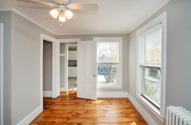 unfurnished room featuring light wood finished floors, crown molding, a ceiling fan, radiator heating unit, and baseboards