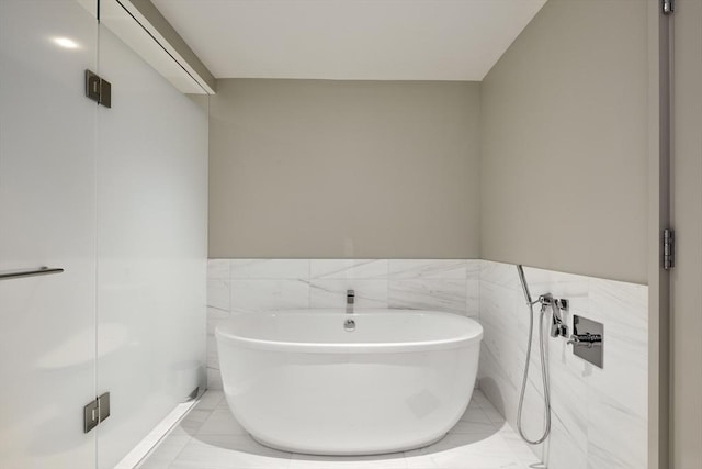 bathroom with tile walls, a washtub, and tile patterned floors