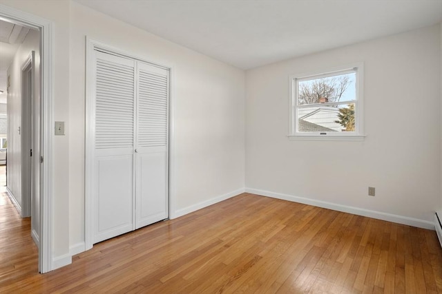 unfurnished bedroom with attic access, light wood-style flooring, baseboards, and a closet