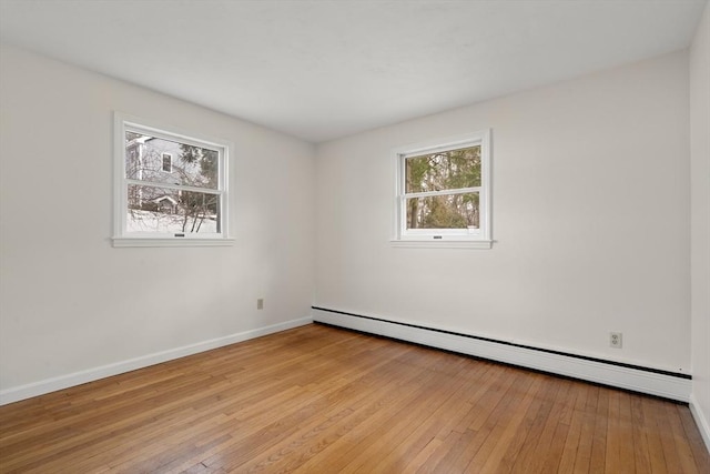 empty room featuring a baseboard heating unit, baseboards, and light wood finished floors