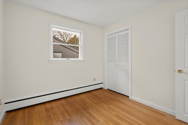 unfurnished bedroom featuring a baseboard radiator, baseboards, a closet, and light wood-style flooring