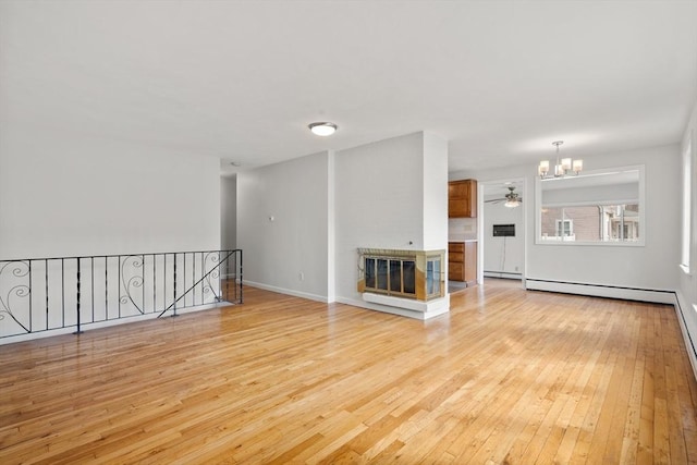 unfurnished living room featuring ceiling fan with notable chandelier, a baseboard heating unit, light wood finished floors, baseboards, and a brick fireplace