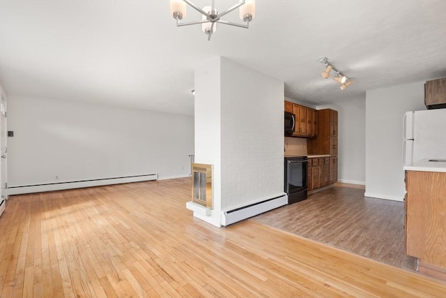 unfurnished living room featuring track lighting, a baseboard heating unit, baseboard heating, light wood-style flooring, and an inviting chandelier