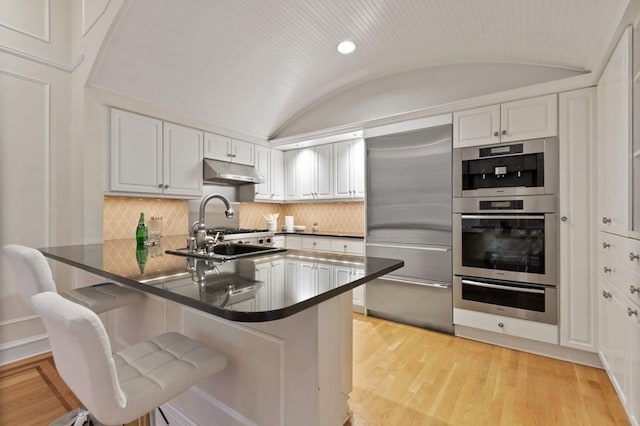 kitchen with white cabinets, stainless steel appliances, lofted ceiling, and brick ceiling