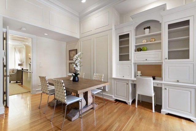 dining space with built in shelves, light wood-type flooring, ornamental molding, and built in desk