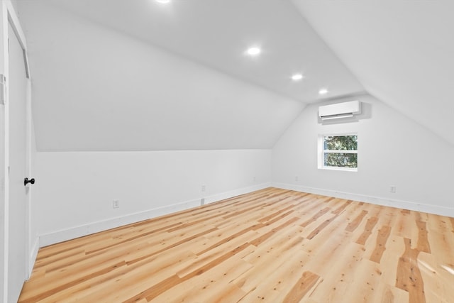 additional living space featuring light hardwood / wood-style floors, an AC wall unit, and lofted ceiling