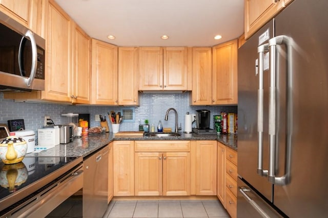 kitchen with dark stone countertops, sink, stainless steel appliances, and light brown cabinetry