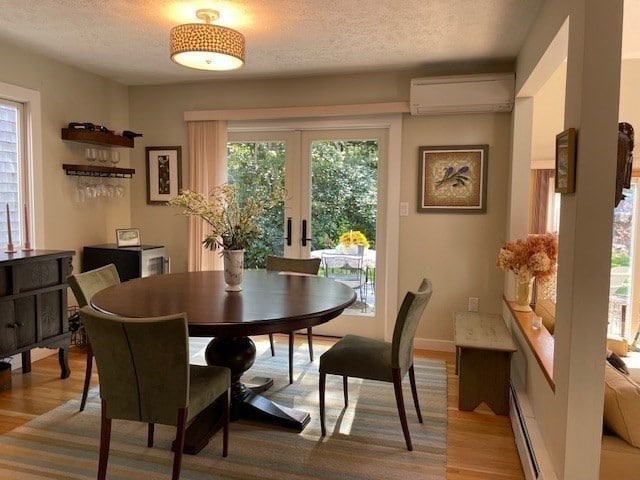 dining room featuring a baseboard heating unit, a wall mounted AC, a textured ceiling, light hardwood / wood-style floors, and french doors