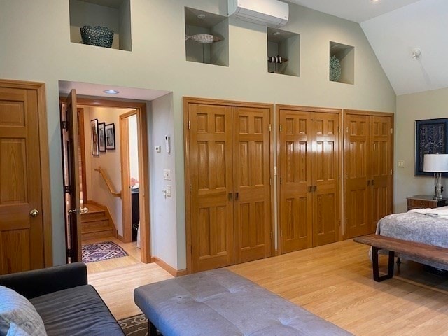 bedroom with multiple closets, high vaulted ceiling, wood-type flooring, and a wall unit AC