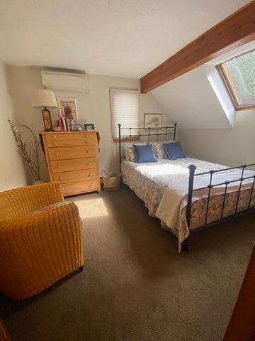 bedroom with an AC wall unit, vaulted ceiling with skylight, and carpet floors