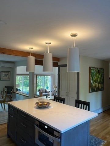 kitchen featuring a wall unit AC, a kitchen island, wood-type flooring, and pendant lighting