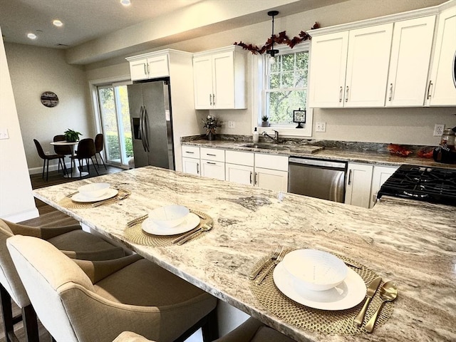 kitchen featuring light stone countertops, appliances with stainless steel finishes, decorative light fixtures, white cabinetry, and a breakfast bar area