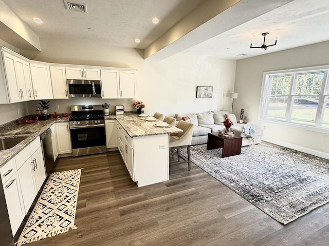 kitchen featuring light stone countertops, stainless steel appliances, kitchen peninsula, a kitchen bar, and white cabinets