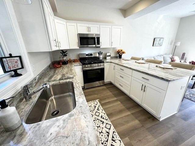 kitchen featuring kitchen peninsula, stainless steel appliances, dark wood-type flooring, sink, and white cabinets