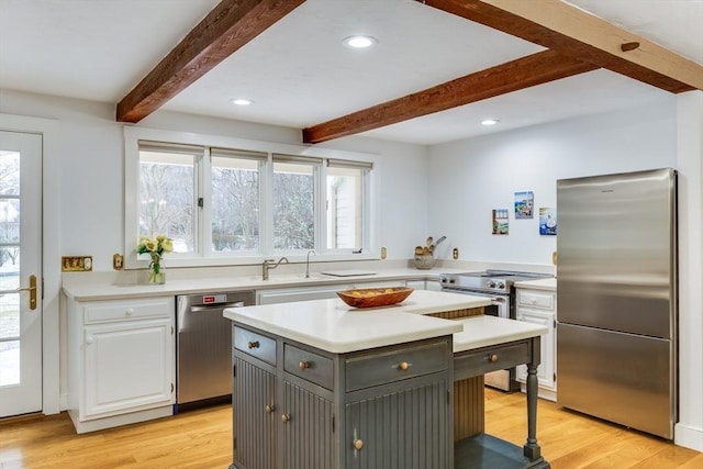 kitchen featuring appliances with stainless steel finishes, light countertops, light wood-style floors, white cabinetry, and beam ceiling