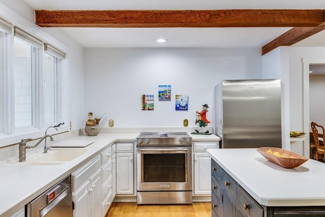 kitchen featuring appliances with stainless steel finishes, a sink, light countertops, white cabinetry, and beam ceiling