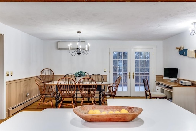 dining room featuring a wainscoted wall, french doors, baseboard heating, a wall mounted air conditioner, and an inviting chandelier