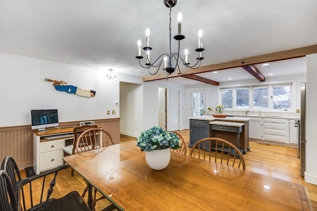 dining space with light wood finished floors, beamed ceiling, and wainscoting