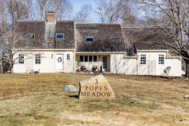 back of house with a shingled roof, a chimney, and a lawn