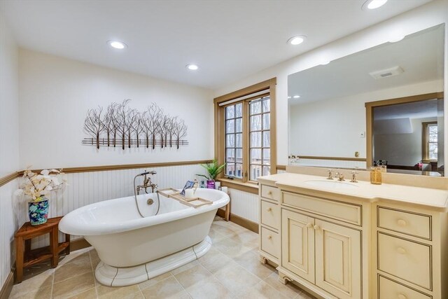 full bath with a wainscoted wall, plenty of natural light, vanity, and a freestanding bath