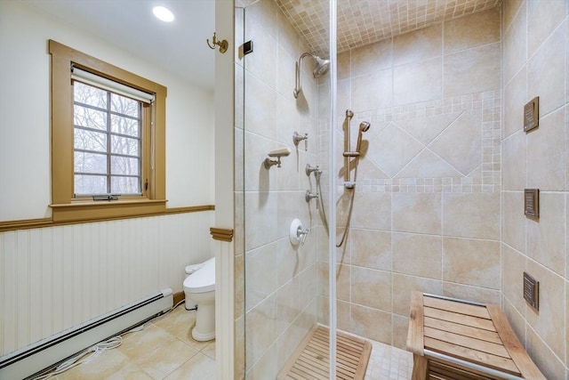 full bath with a baseboard radiator, tile patterned flooring, toilet, a wainscoted wall, and tiled shower