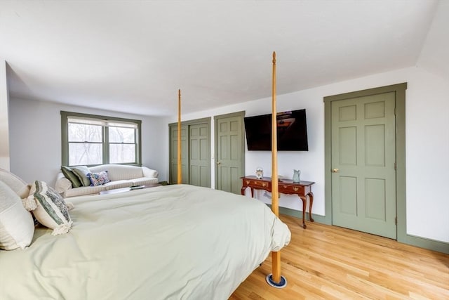 bedroom featuring light wood-style floors, baseboards, and multiple closets