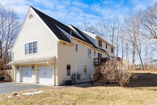 exterior space with aphalt driveway, ac unit, a yard, a garage, and stairs