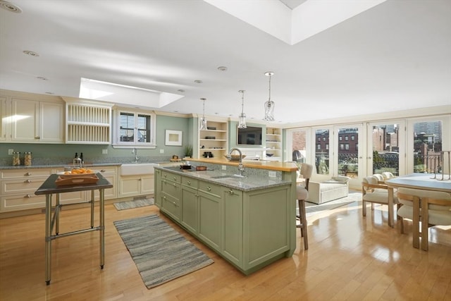 kitchen with light stone countertops, green cabinets, sink, and a kitchen island with sink