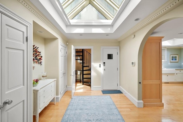 interior space with light hardwood / wood-style floors, a tray ceiling, ornamental molding, and a skylight