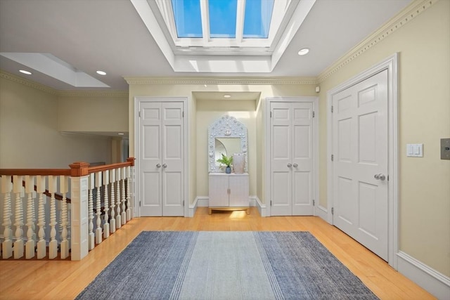 foyer entrance featuring a skylight, a raised ceiling, ornamental molding, and light hardwood / wood-style flooring