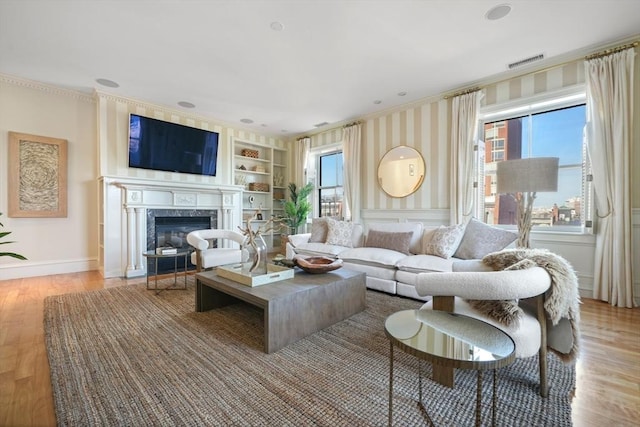 living room featuring a high end fireplace, built in features, crown molding, and light hardwood / wood-style flooring