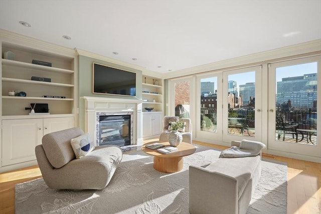 living room with a fireplace, built in shelves, crown molding, and light wood-type flooring