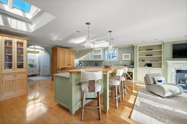 kitchen featuring a high end fireplace, ornamental molding, light hardwood / wood-style flooring, and a center island with sink