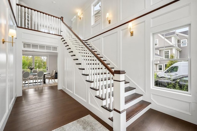 stairs featuring wood-type flooring, a decorative wall, and a high ceiling