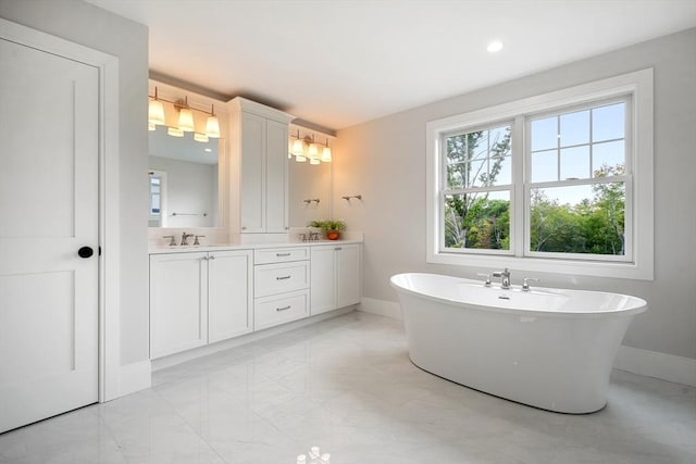 bathroom featuring marble finish floor, baseboards, a freestanding bath, and vanity