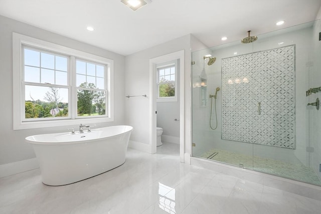 bathroom with a stall shower, a freestanding tub, toilet, and baseboards