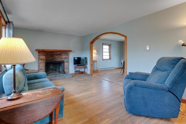 living area featuring a brick fireplace, light wood-style flooring, arched walkways, and a baseboard radiator