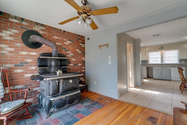 living area featuring visible vents, brick wall, baseboards, light wood-type flooring, and a wood stove