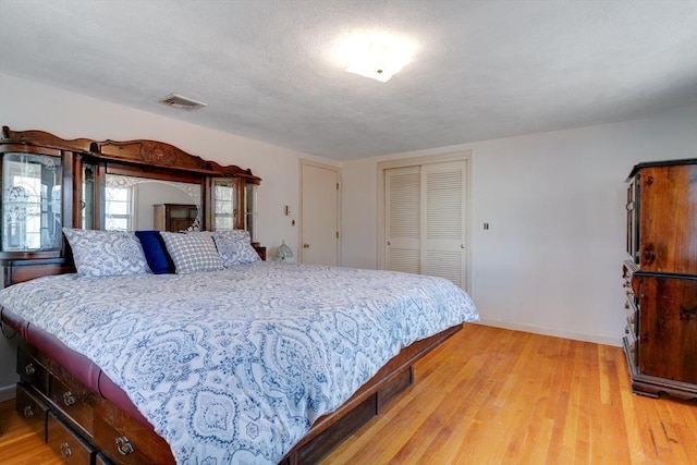 bedroom with light wood-style flooring, baseboards, visible vents, and a closet