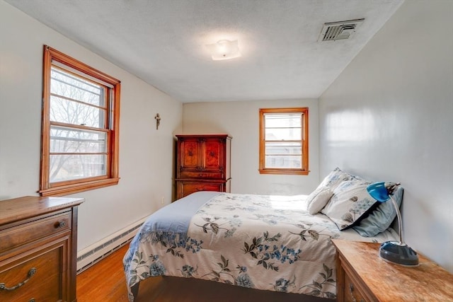 bedroom with a baseboard heating unit, visible vents, and light wood-type flooring