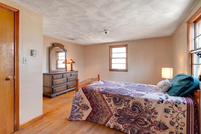 bedroom with visible vents, baseboards, light wood-type flooring, and a textured ceiling