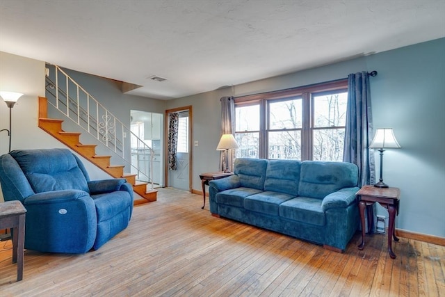 living room with visible vents, baseboards, light wood-style floors, and stairs