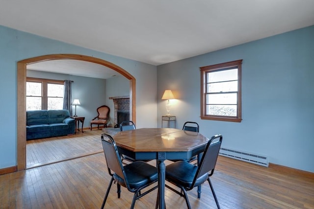 dining space with baseboards, a baseboard radiator, a fireplace, arched walkways, and wood-type flooring