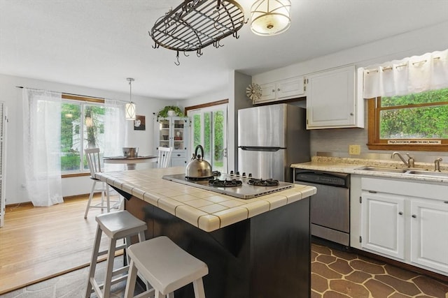 kitchen featuring a sink, white cabinetry, a center island, tile counters, and appliances with stainless steel finishes