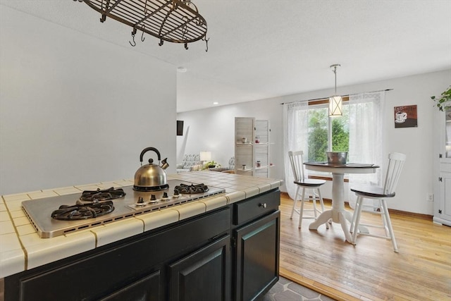 kitchen featuring tile counters, light wood-style floors, dark cabinets, and stainless steel gas cooktop
