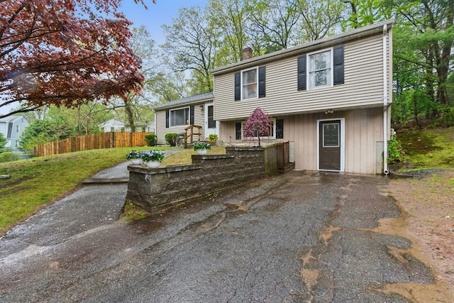 tri-level home with a chimney, a front lawn, and fence
